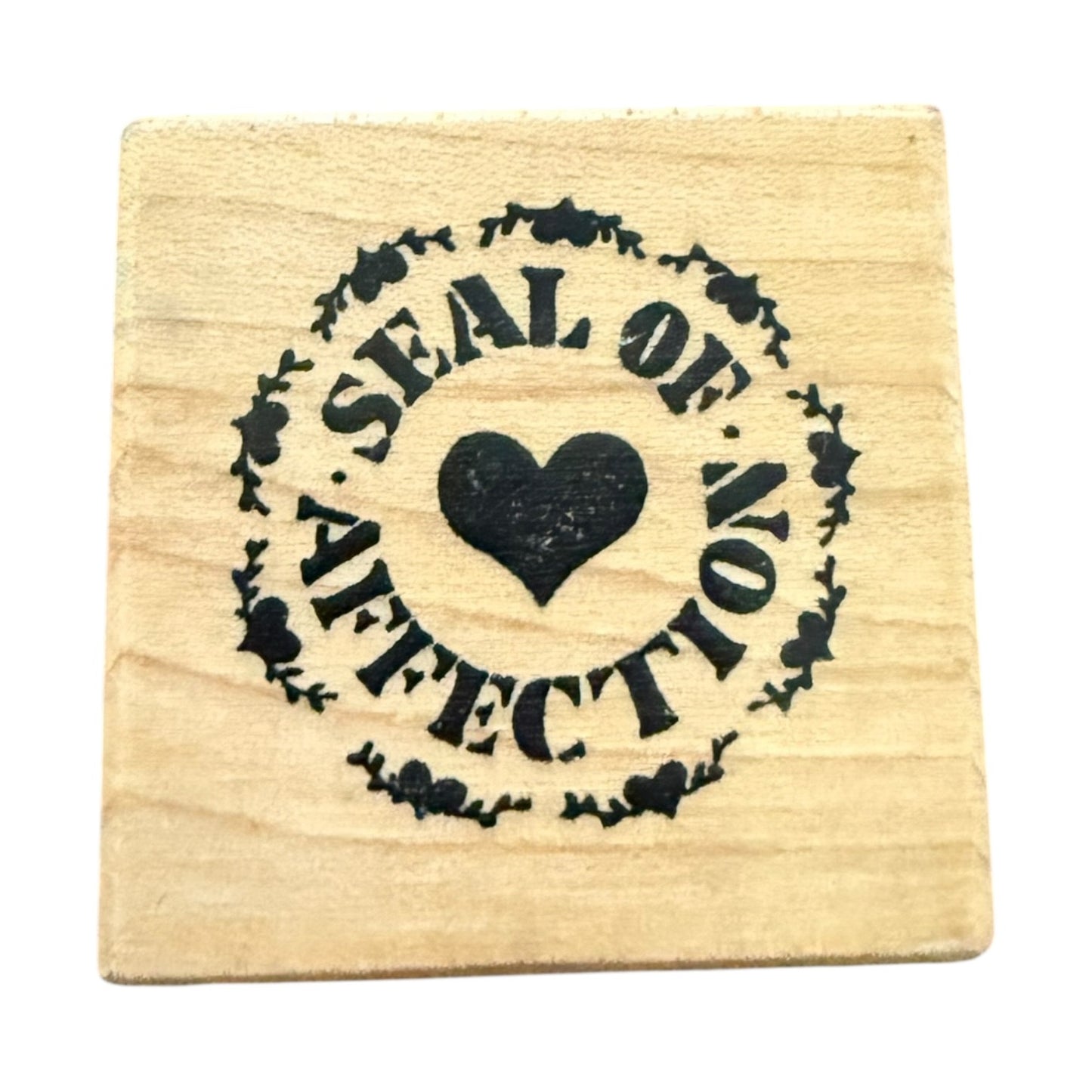 A square wooden rubber stamp with a black printed design that reads 'SEAL OF AFFECTION' around a central heart, shown on a plain white background.