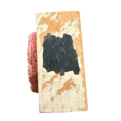 A rectangular wooden stamp block with a distressed finish with a black mark all set against a plain white background.