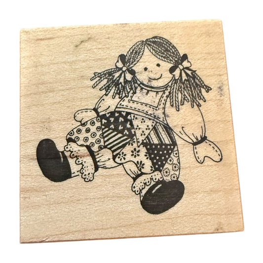 Wooden stamp with a black illustration of a patchwork doll on a beige background