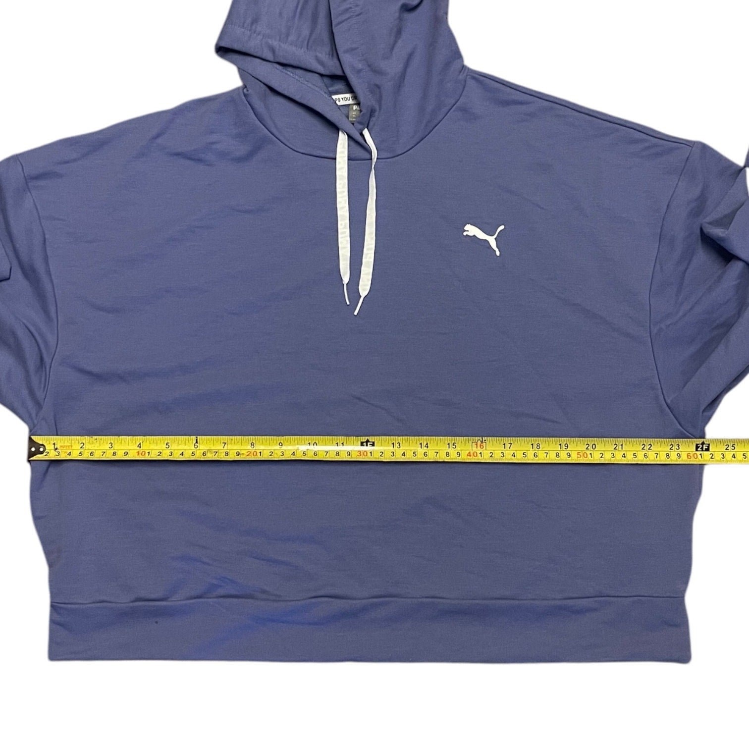 A Puma pullover hoodie with white drawstrings and a white Puma logo on the chest, shown with a yellow tape measure stretched horizontally across the waist to indicate the garment's size.