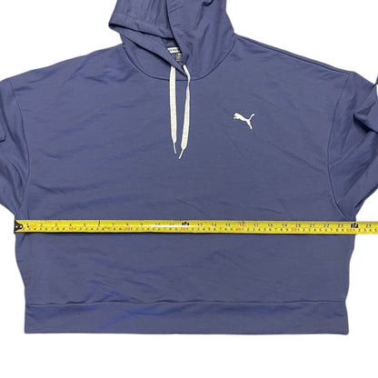 A Puma pullover hoodie with white drawstrings and a white Puma logo on the chest, shown with a yellow tape measure stretched horizontally across the waist to indicate the garment's size.