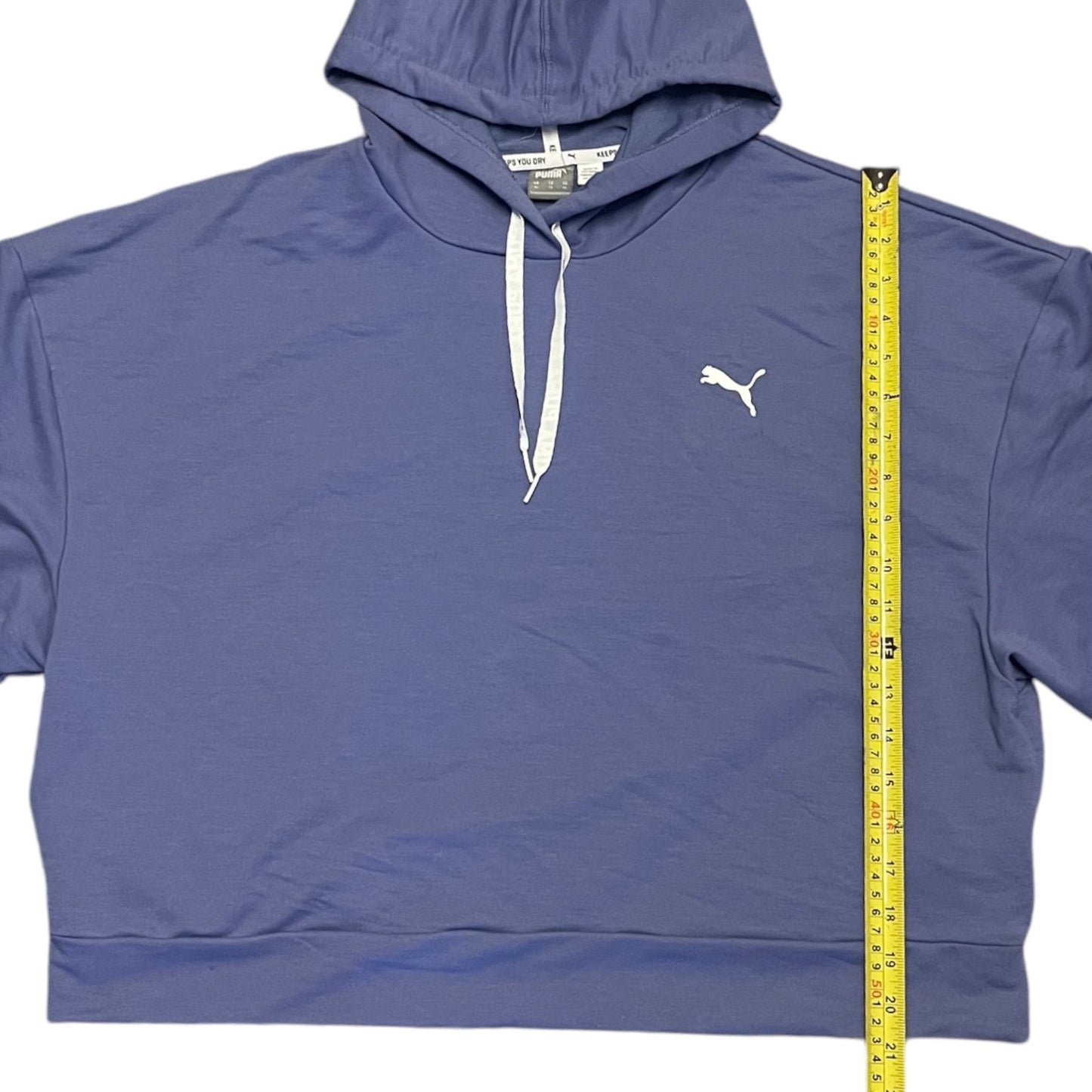 A Puma cropped hoodie laid flat on a white background, with a yellow measuring tape standing vertically next to it to show the height.