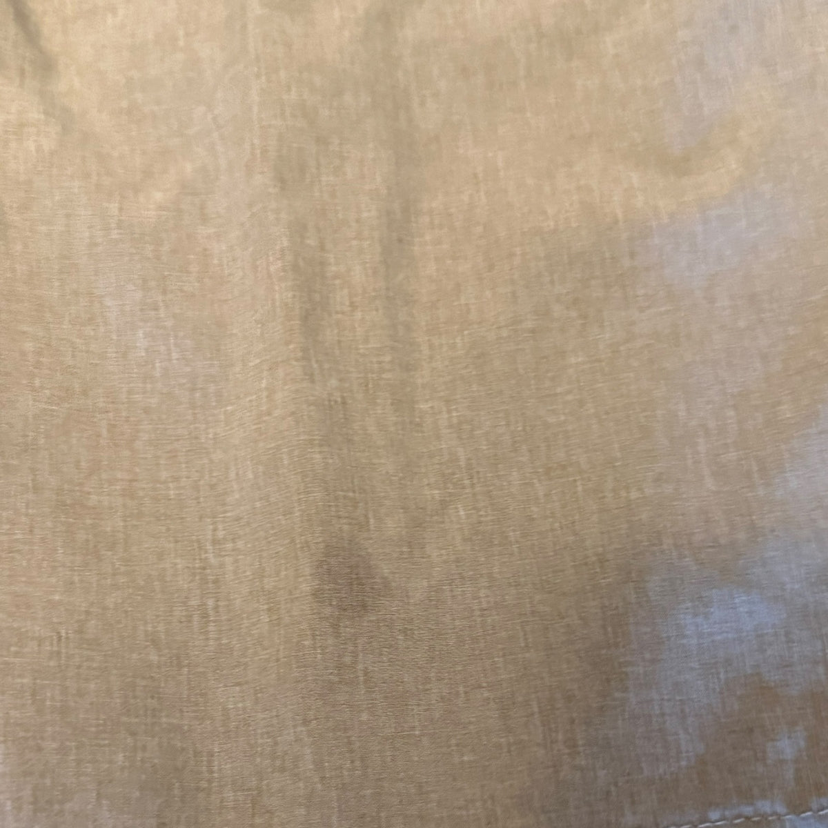 A close-up of a light beige woven fabric with a visible stain.