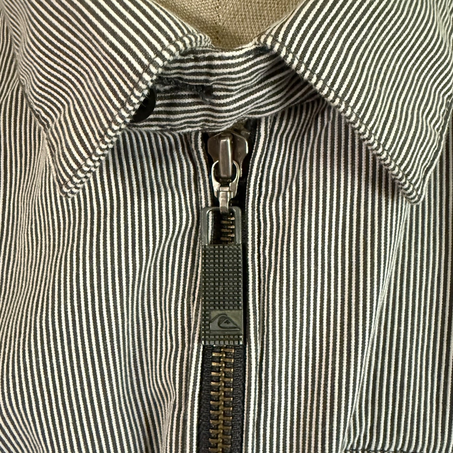 Close-up of a zipper on a striped jacket with a brand logo.