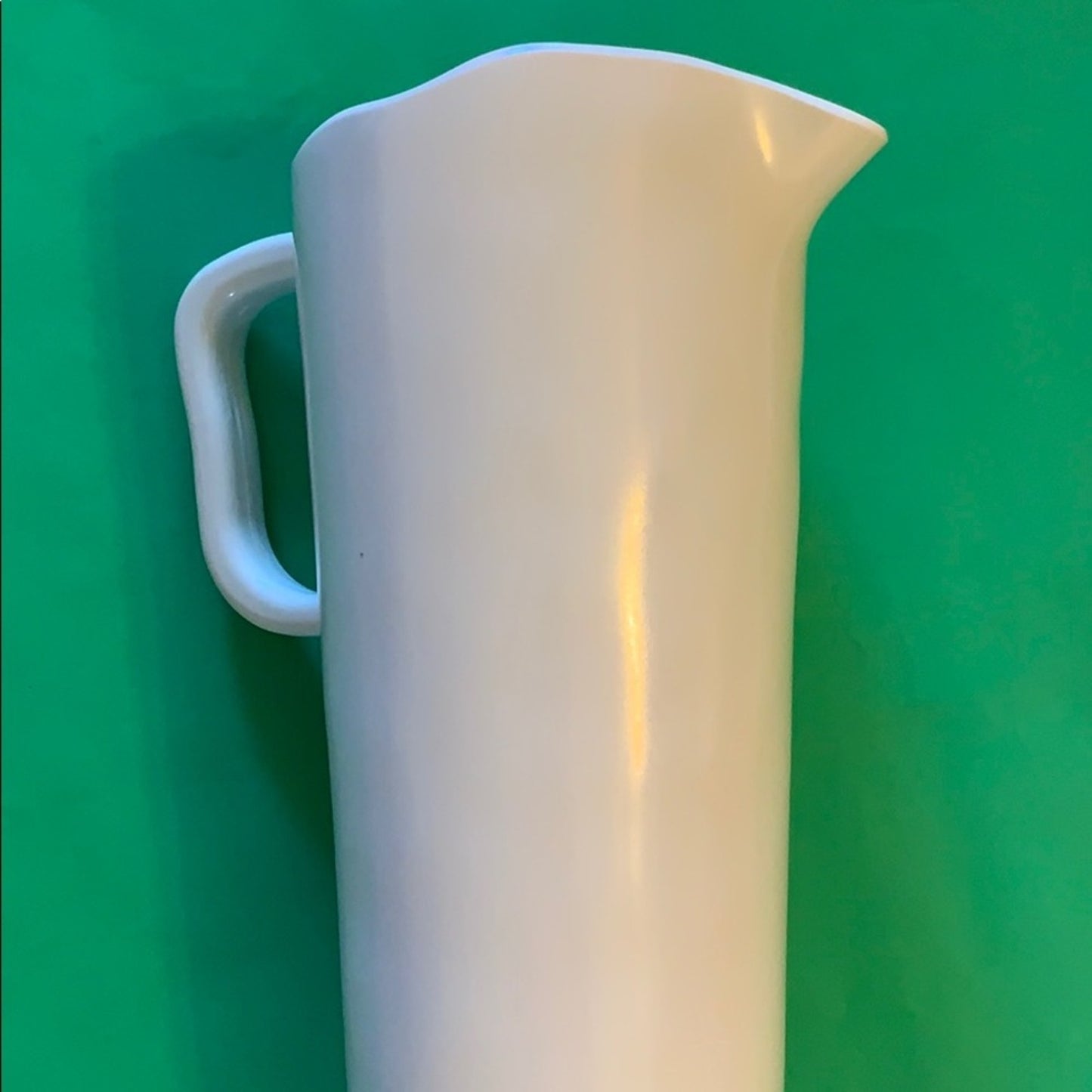 A white pitcher with a curved handle and pouring spout, shown against a solid green background.