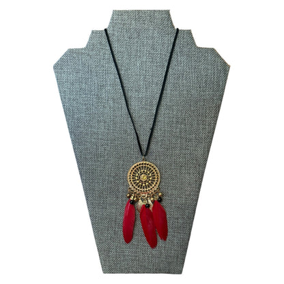 Necklace with red feathers and gold circular pendant on a gray stand