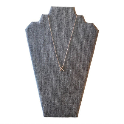 A delicate rose gold toned necklace with an X-shaped pendant displayed on a textured gray jewelry bust against a white background.