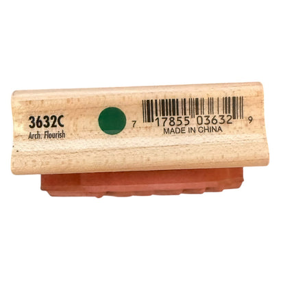 A wooden rubber stamp with a green ink dot, featuring printed text including '3632C Arch. Flourish' and a barcode on the light wood handle, with the reddish-brown rubber seal visible underneath.