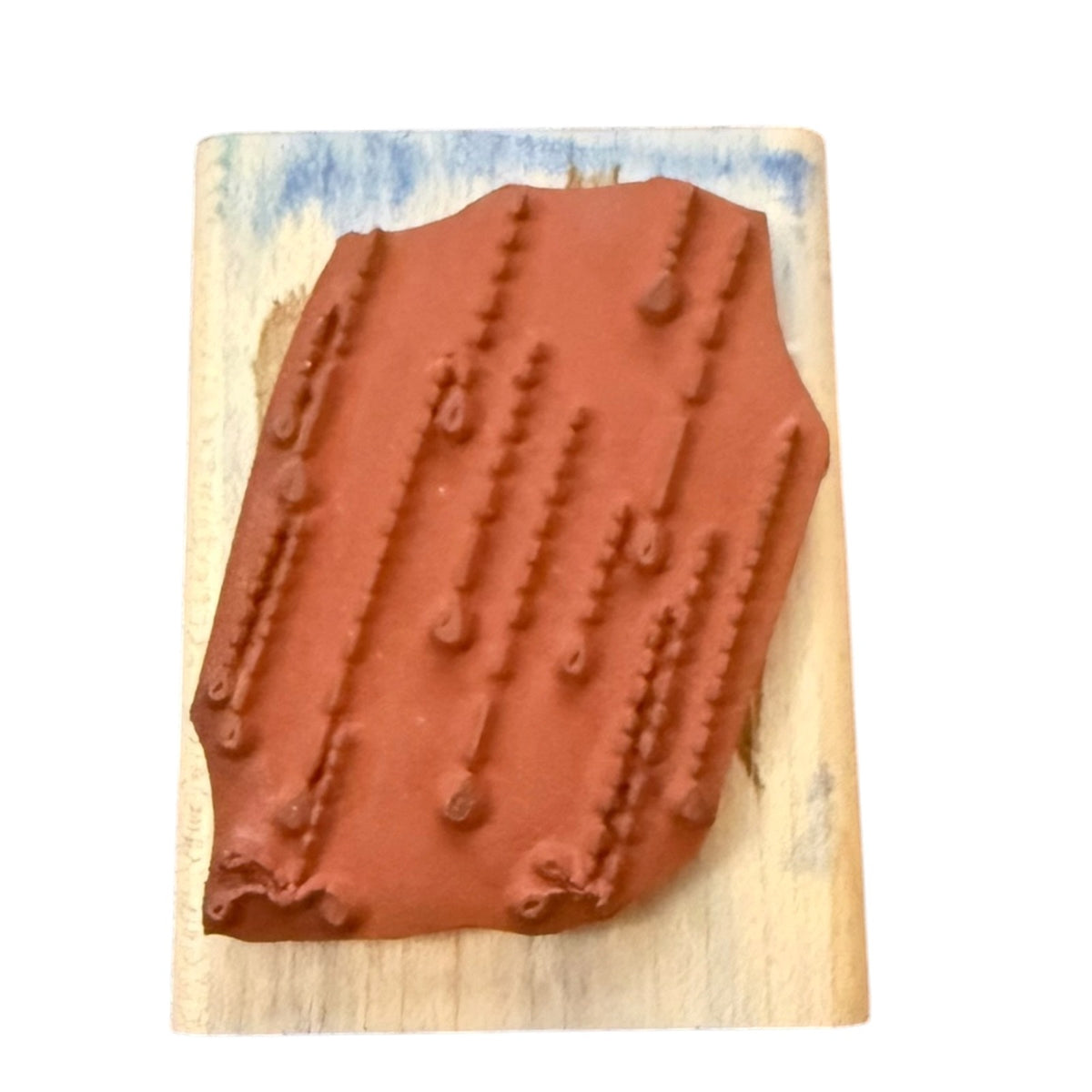 A terracotta-colored rubber stamp with falling rain patterns, mounted on a rectangular light wood block with blue painted accents, shown against a plain white background.