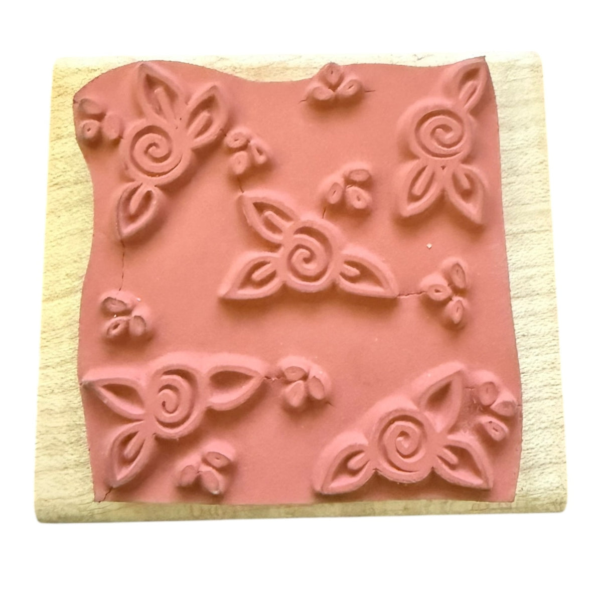 A rubber stamp block with embossed floral and scroll motifs, mounted on a light-colored wooden square against a white background.