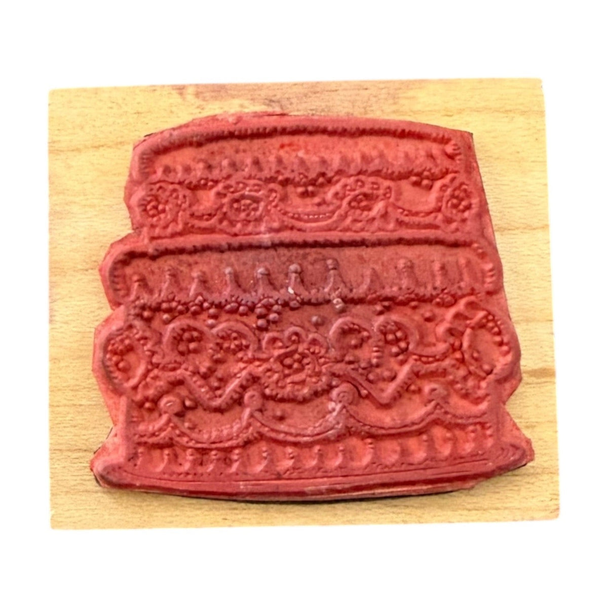 A red decorative embossed rubber stamp on a light wood block, shown against a plain white background.