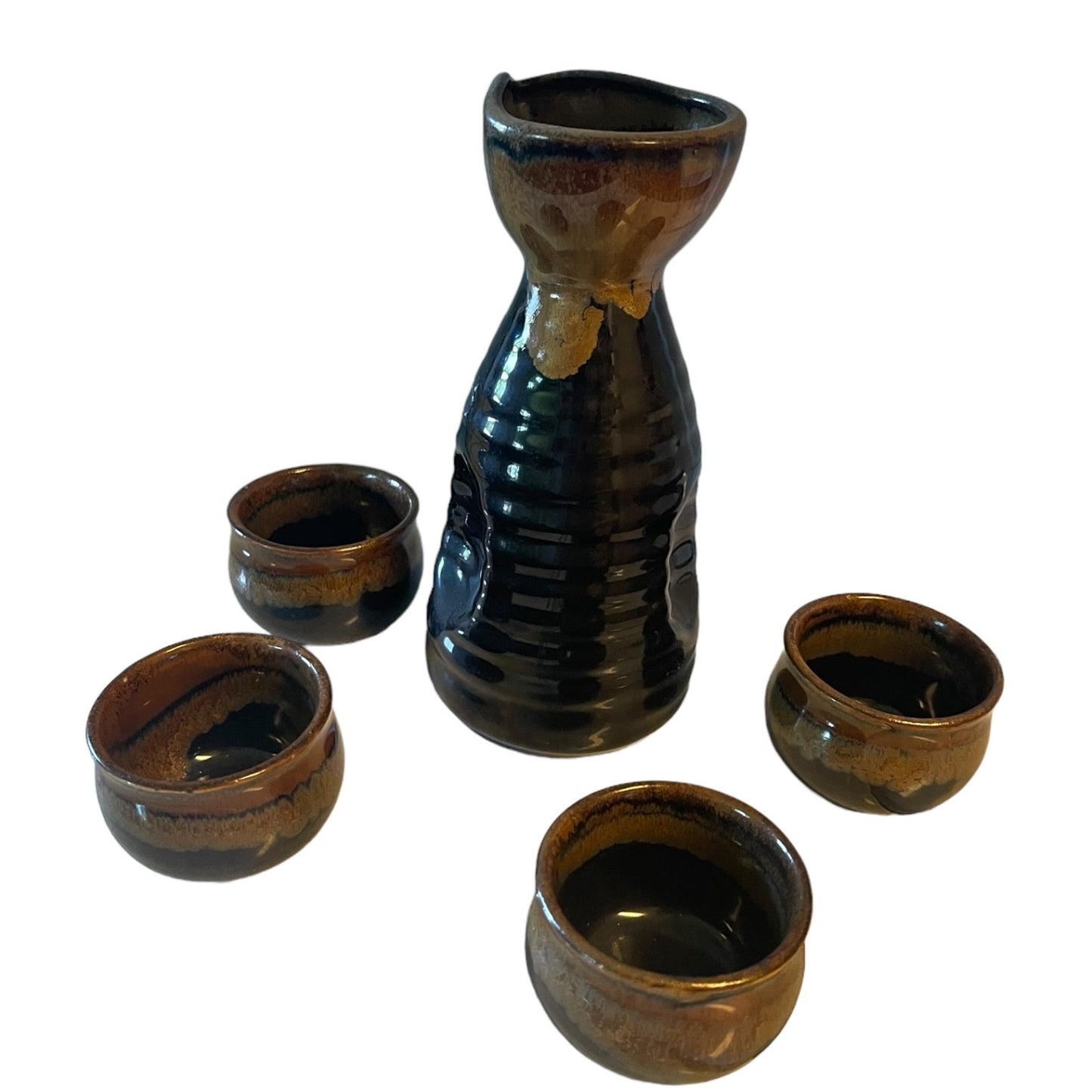 A ceramic sake set featuring a tall ribbed carafe and four small matching cups with a glossy dark brown and black glaze, shown on a plain white background.
