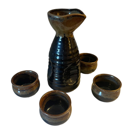 A ceramic sake set featuring a tall carafe and four small cups with a glossy dark brown and black glaze, set against a plain white background.