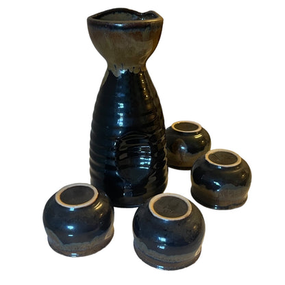 A ceramic sake set featuring a tall, ribbed sake holder in a glossy black glaze with a natural brown edge, accompanied by four matching small tumblers, all photographed on a plain white background.