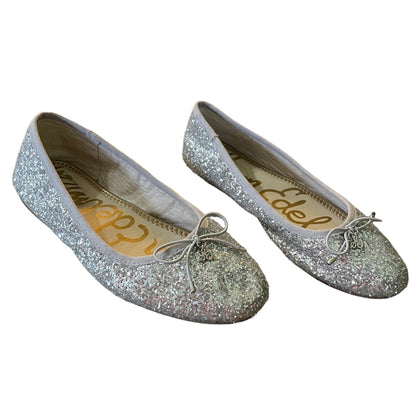 A pair of silver glitter ballet flats with small bow details on the toes, shown against a plain white background. 