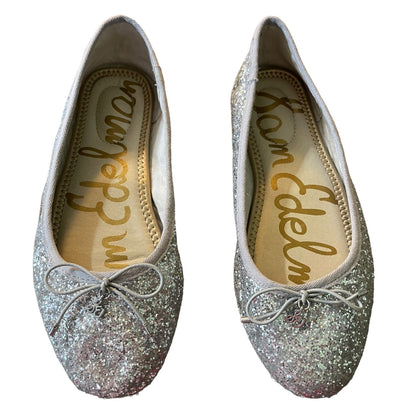 A pair of silver glitter ballet flats with a small bow on the toe, shown from both the top and side views against a white background. The insole features the 'Sam Edelman' brand name in gold script.