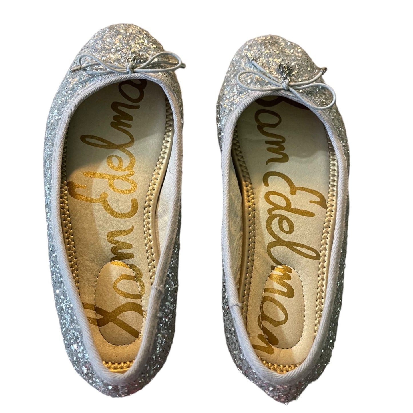 A pair of silver glitter ballet flats with small bow details on the toes, shown from a top-down view on a white background. The insoles feature the brand name 'Sam Edelman' in gold script.