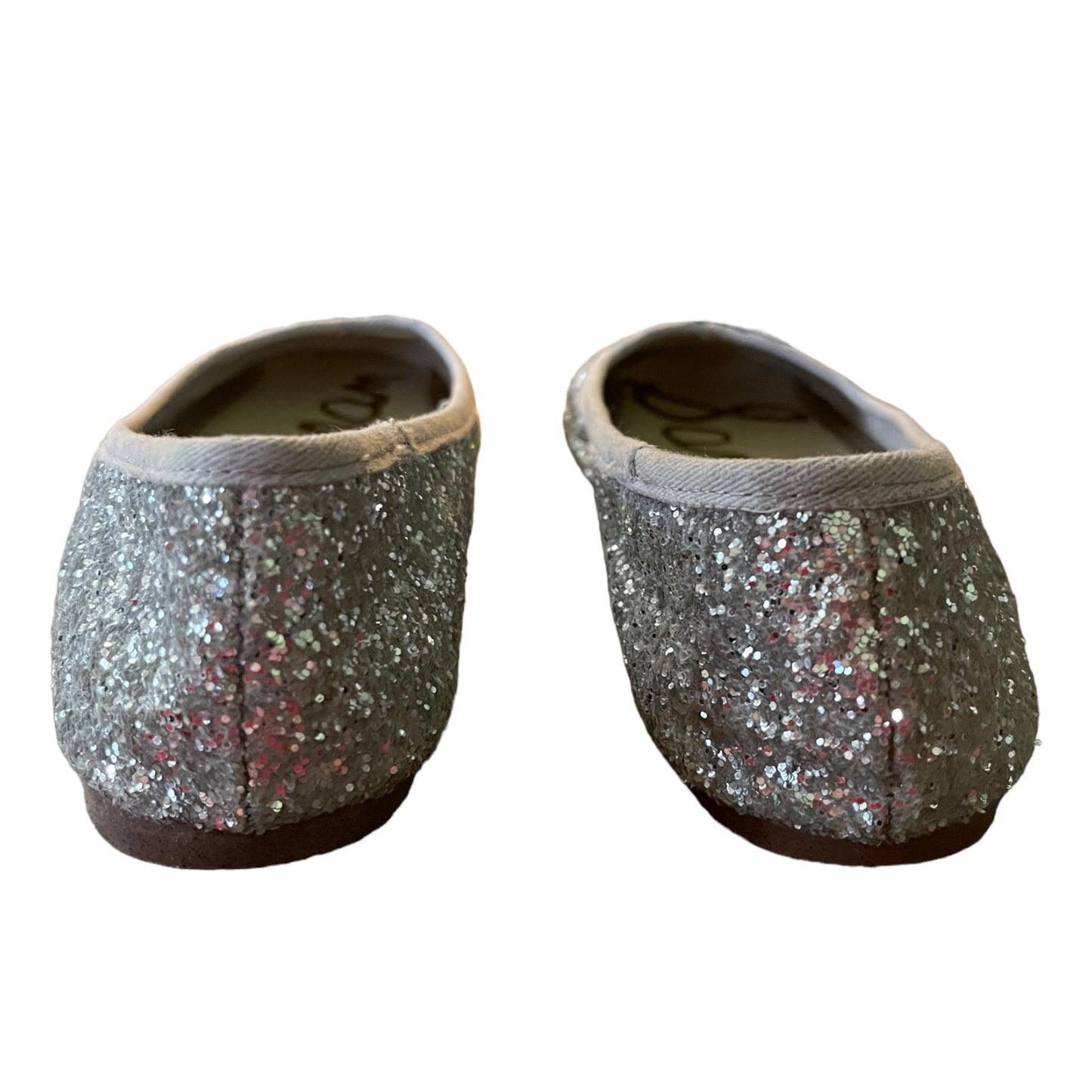A pair of slip-on flats covered in silver glitter, shown from the back on a plain white background.