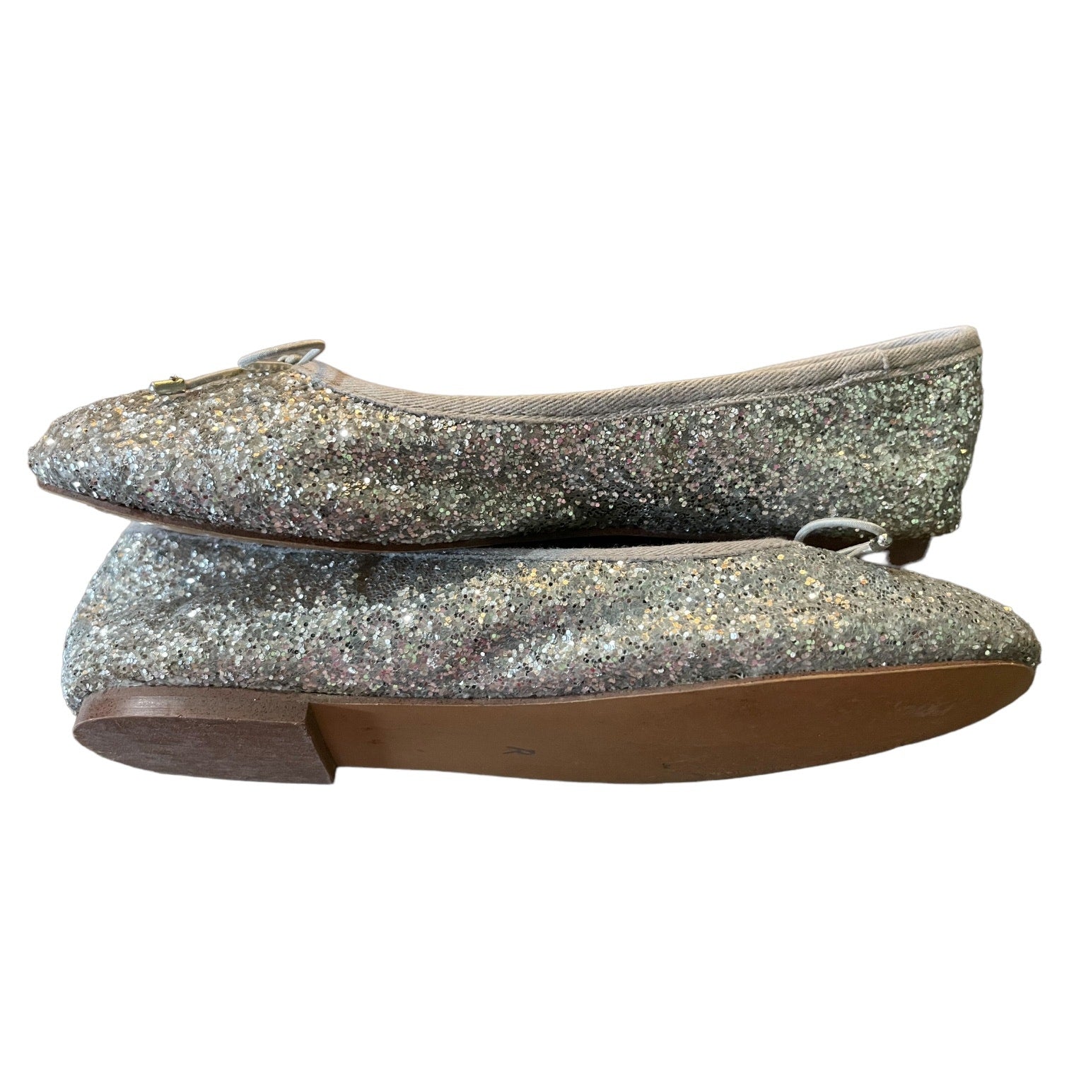 A pair of glittery silver ballet flats with a small bow detail on the toe, shown against a plain white background.