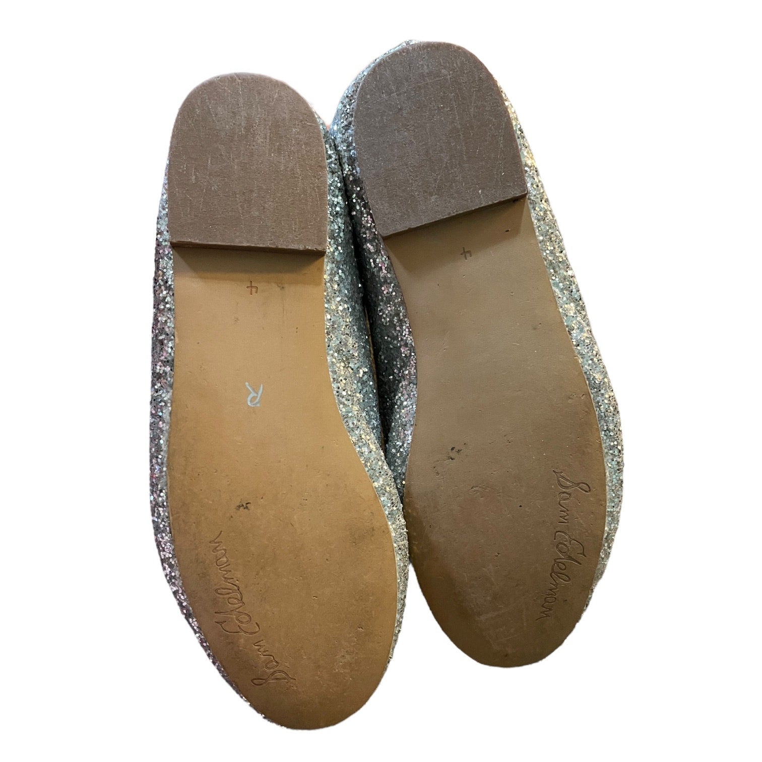 A pair of flats shown from the bottom, featuring silver glitter uppers with a tan sole and a brown heel cap, on a white background.