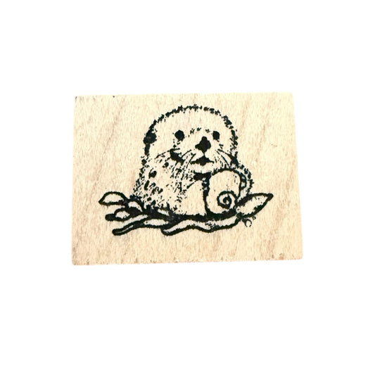 Rubber stamp with a design of a sea otter holding a shell on a beige background