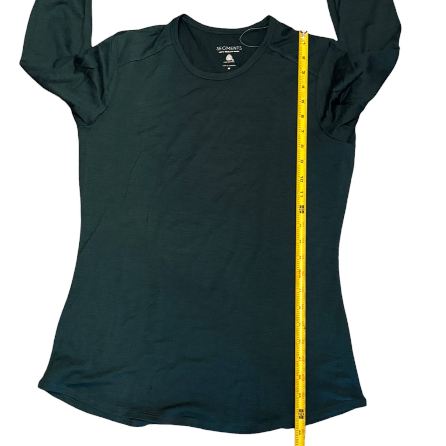 A dark green long-sleeve shirt laid flat on a white background, with a yellow measuring tape running vertically down the side to show the garment's length.