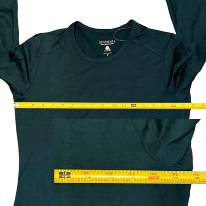 A dark green long-sleeve shirt laid flat on a white background, with a yellow tape measure placed horizontally across the chest and another tape measure along the bottom hem to show garment dimensions.