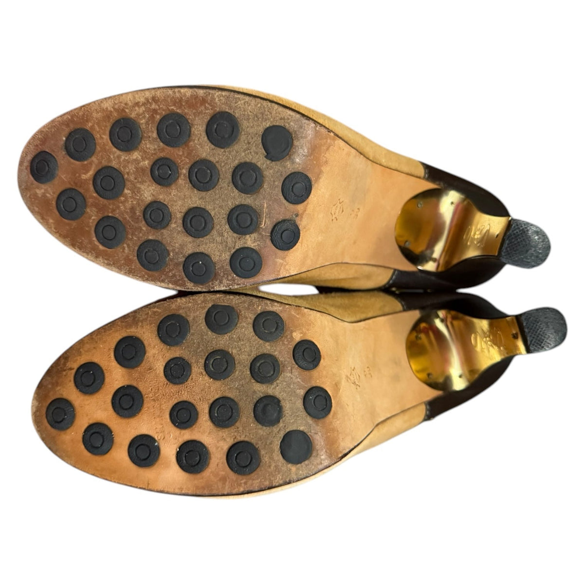 Top-down view of a pair of women's pointed-toe heeled boots showing the tan leather soles with circular black non-slip pads and metallic gold heel caps on a white background.