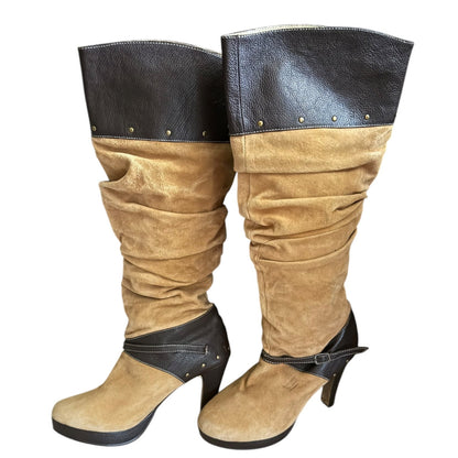 A pair of slouchy knee-high boots in tan suede with brown faux-leather trim at the top and around the ankles, shown on a plain white background.