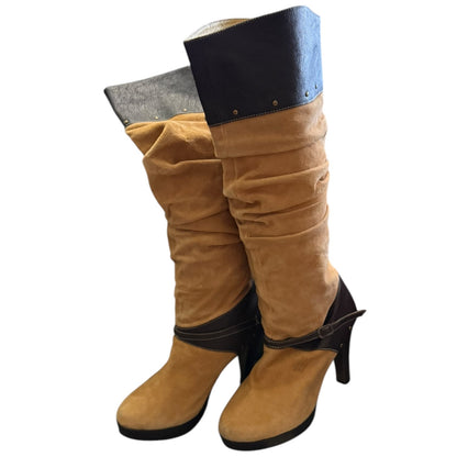 A pair of slouchy knee-high boots in tan suede, dark brown ankle straps, and high stiletto heels, shown against a plain white background.