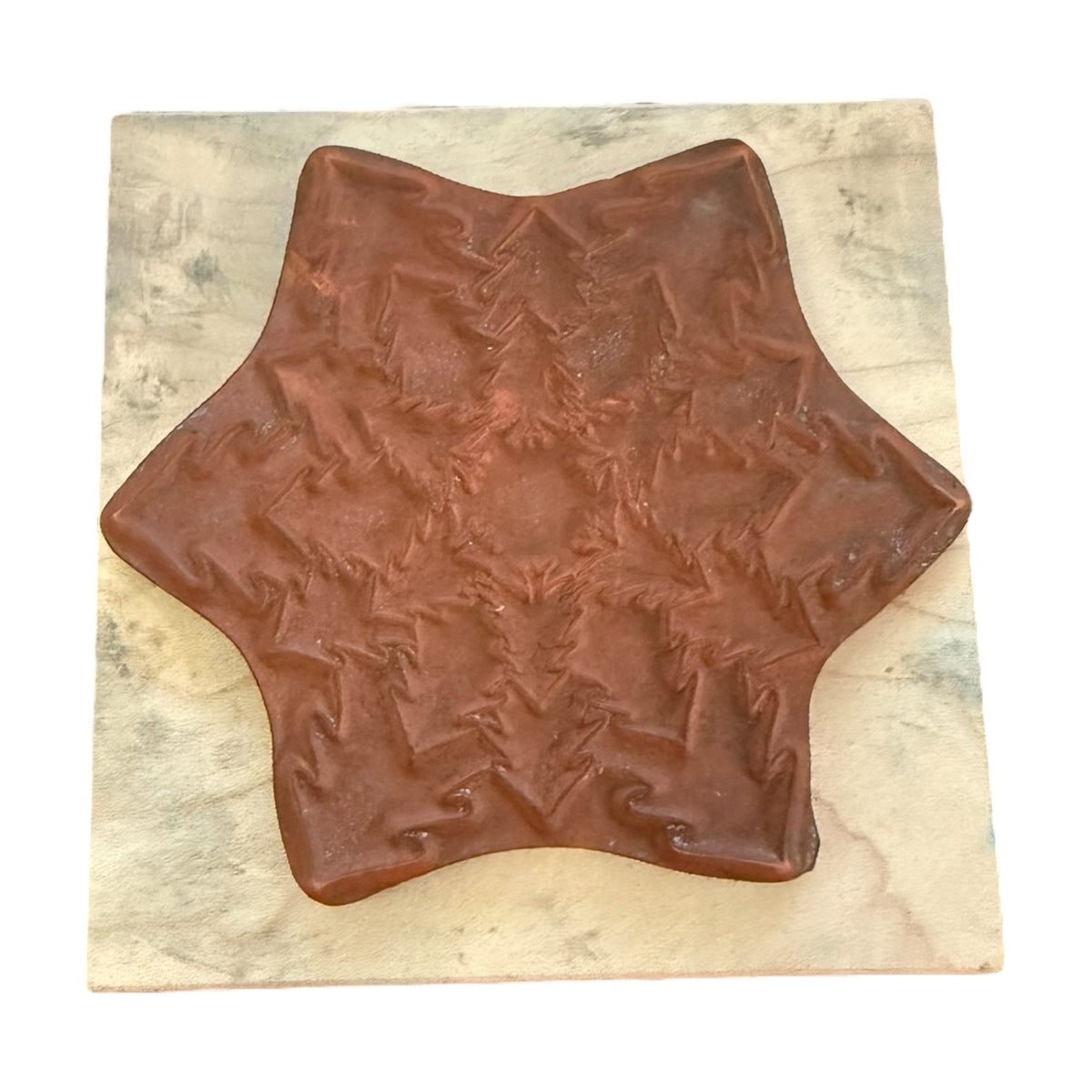 A brown, star-shaped decorative rubber stamp with a textured, embossed pattern, displayed on a square beige marble tile against a white background.