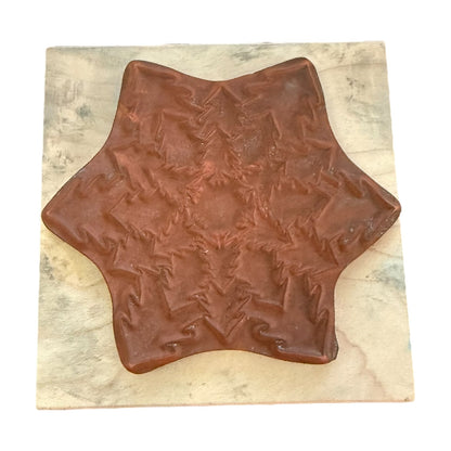 A brown, star-shaped decorative rubber stamp with a textured, embossed pattern, displayed on a square beige marble tile against a white background.
