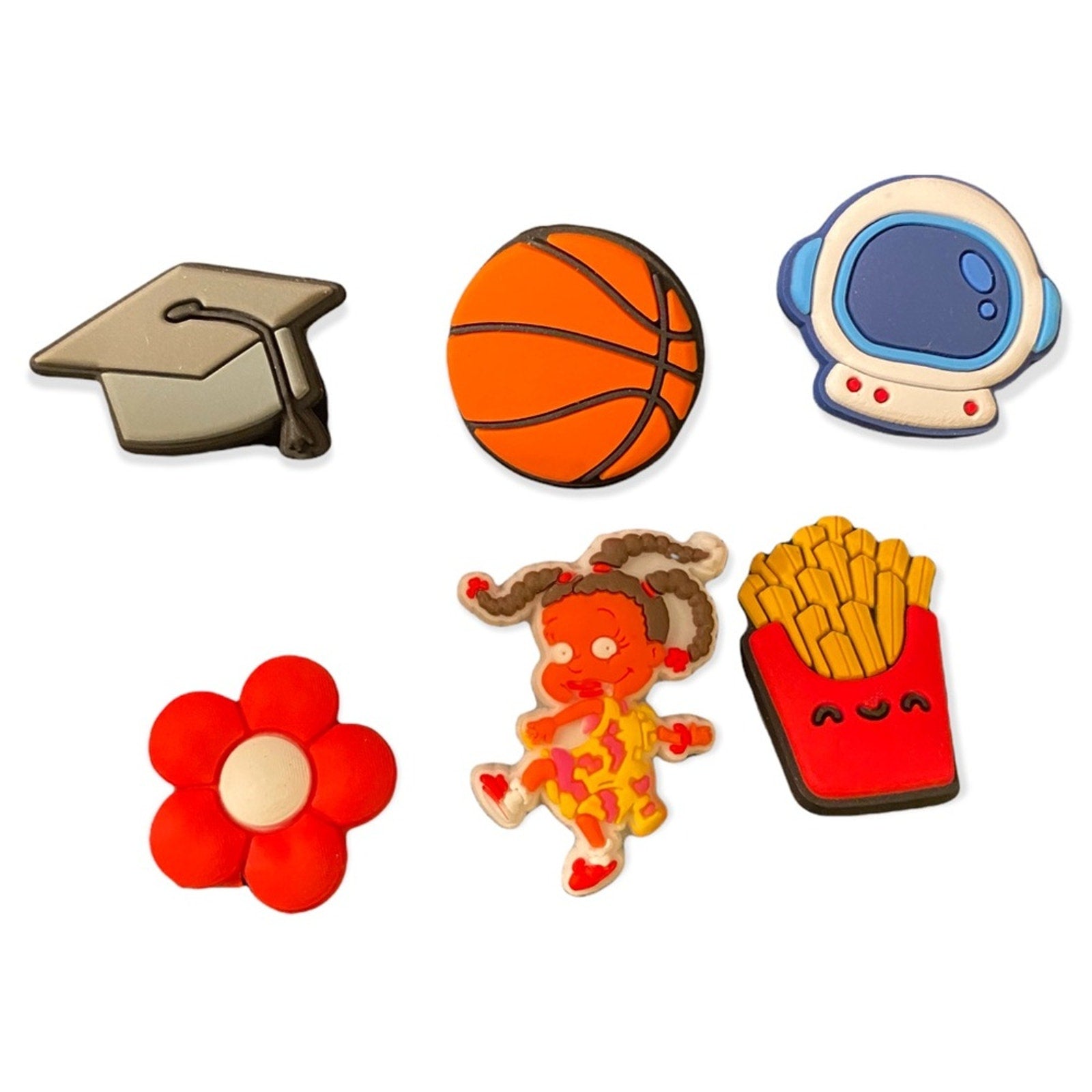 Six colorful shoe charms on a plain white background: a graduation cap, an orange basketball, a white astronaut helmet, a red flower, a dancing girl in a patterned dress, and a red french fries box.