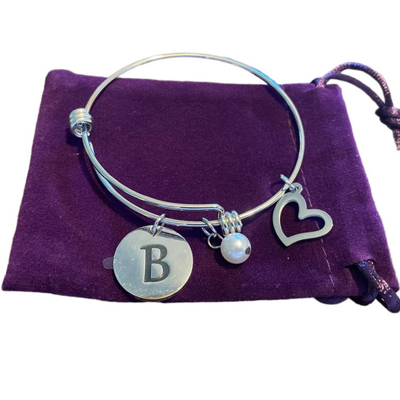 Silver bracelet with heart, letter 'B' charm, and pearl on a purple fabric background