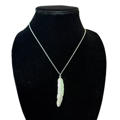 A silver chain necklace with a silver feather pendant, displayed on a black velvet jewelry bust against a white background.