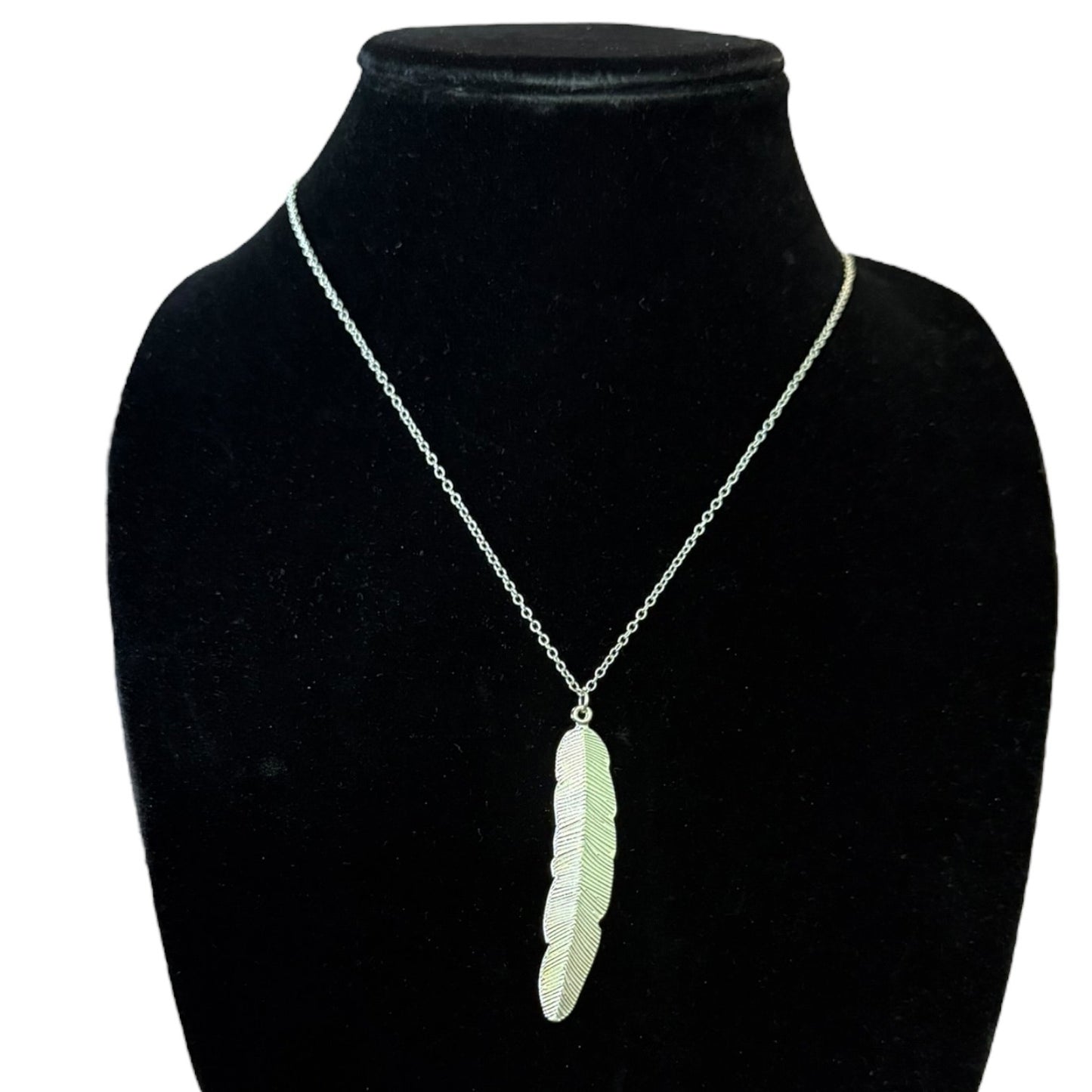 A silver chain necklace with a textured feather pendant, displayed on a black velvet jewelry bust against a white background.