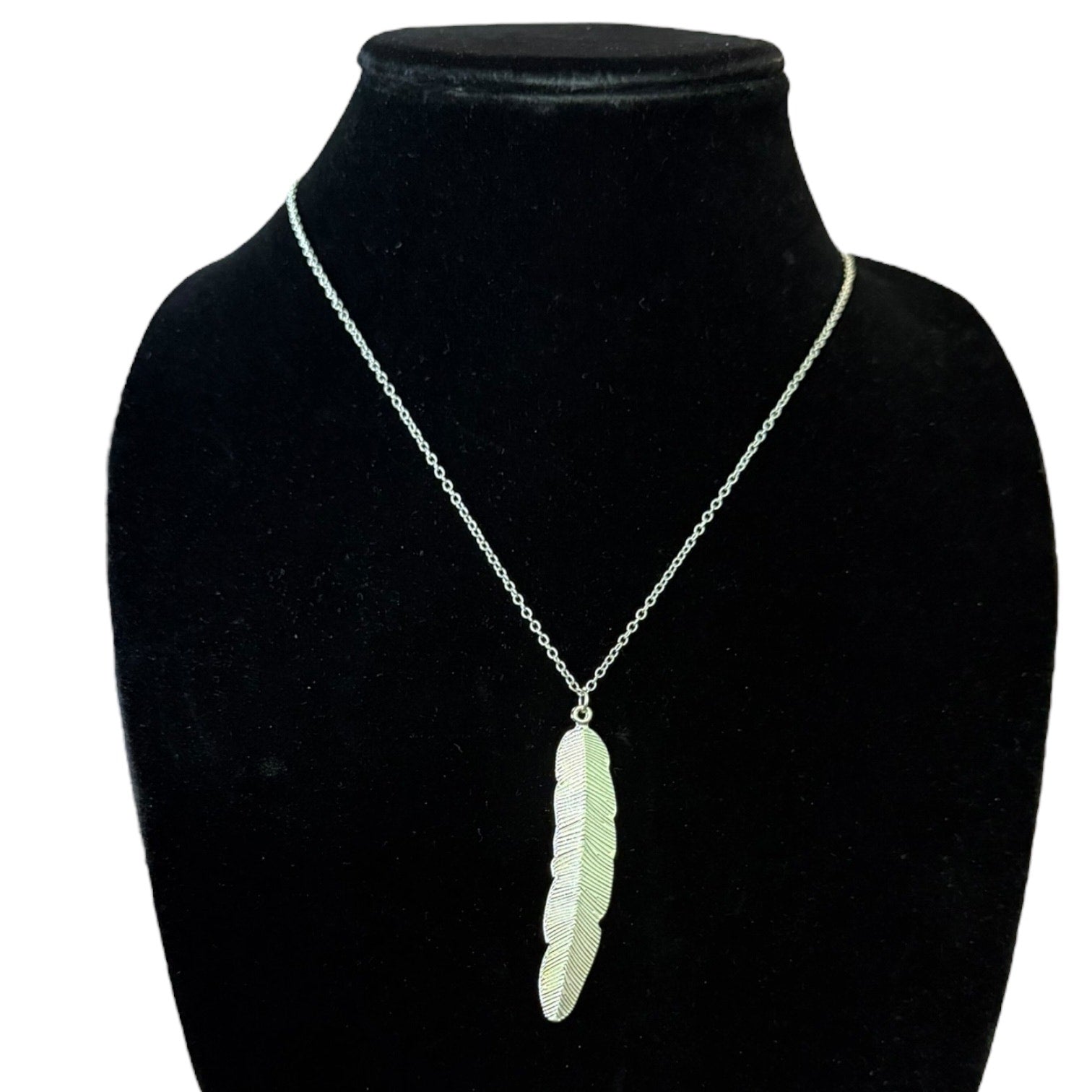 A silver chain necklace with a textured feather pendant, displayed on a black velvet jewelry bust against a white background.