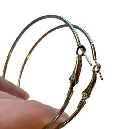 silver-toned metal hoop earrings with spring-ring closures, shown being held by a hand against a plain white background.
