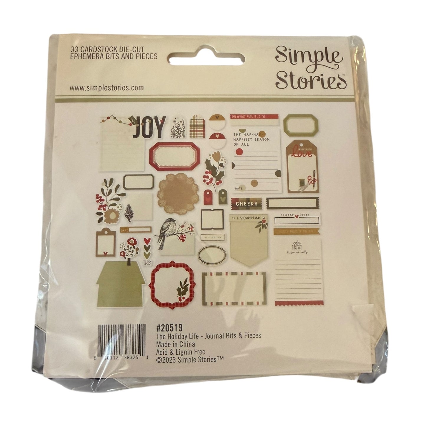 Simple Stories 'The Holiday Life' journaling bits and pieces set in its original plastic packaging, featuring various vintage-style labels, frames, and decorative elements.