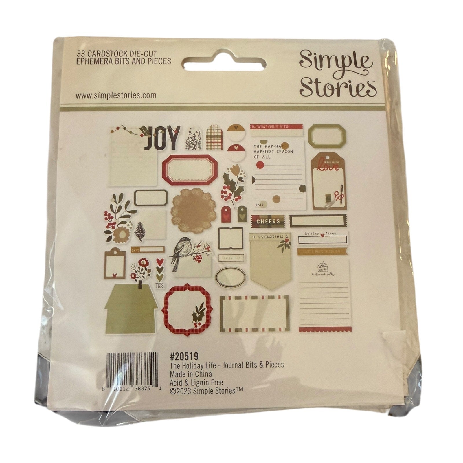 Simple Stories 'The Holiday Life' journaling bits and pieces set in its original plastic packaging, featuring various vintage-style labels, frames, and decorative elements.