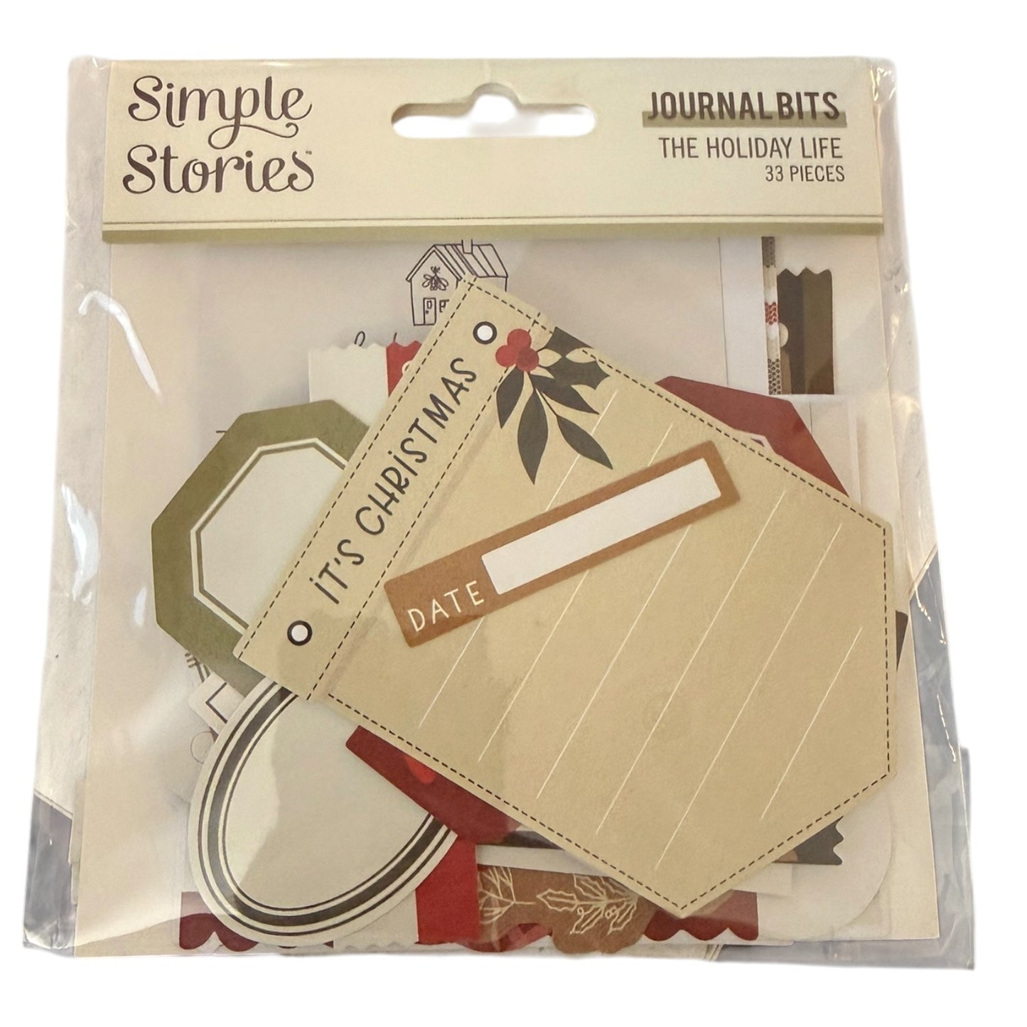 A package of Simple Stories Journal Bits 'The Holiday Life' set, containing 33 pieces of scrapbooking paper and embellishments in a clear plastic bag with a beige header card.