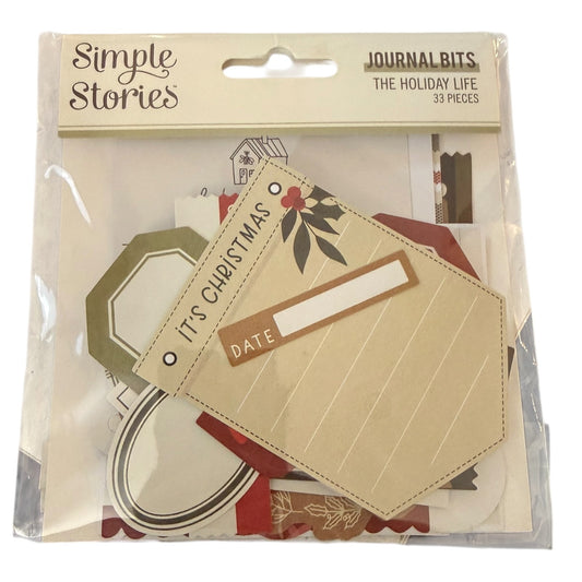 A package of Simple Stories Journal Bits 'The Holiday Life' set, containing 33 pieces of scrapbooking paper and embellishments in a clear plastic bag with a beige header card.