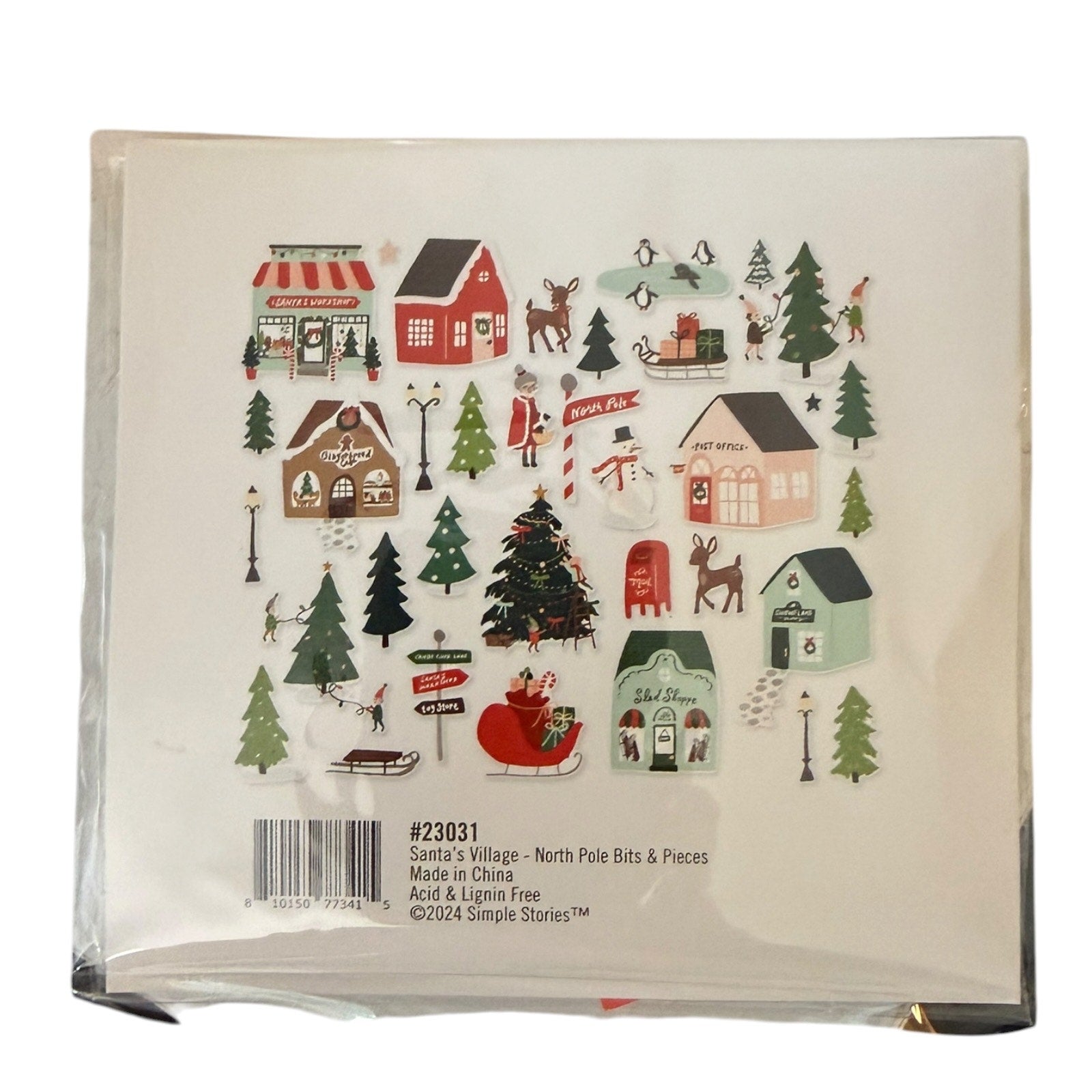A packaged set of Christmas-themed North Pole bits and pieces from Simple Stories, featuring illustrated holiday houses, trees, a Santa Claus sleigh, a snowman, penguins, and other festive details on a white backing card.