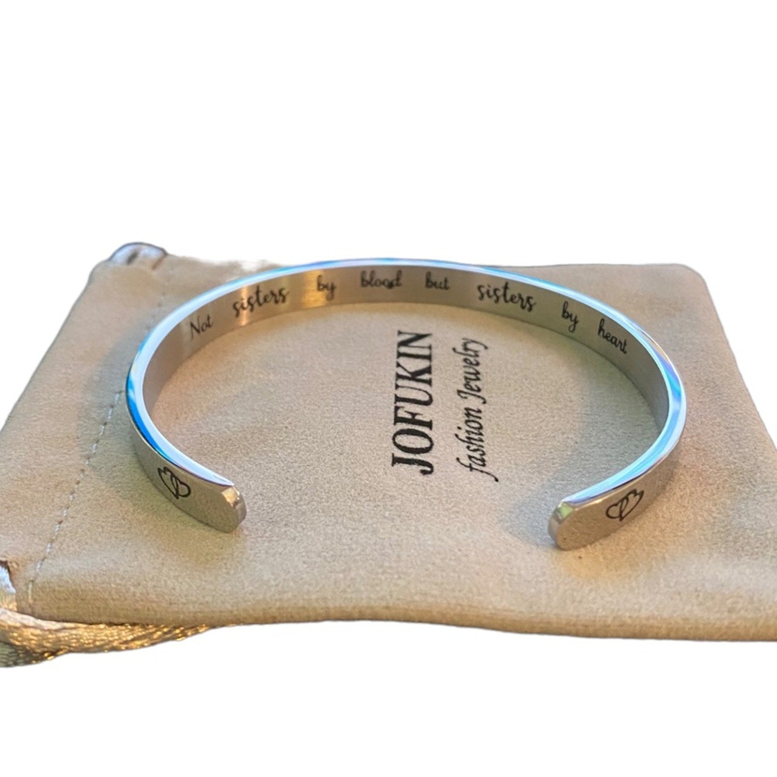 Silver bracelet with engraved text on a beige jewelry pillow, featuring the brand 'JOFUKIN'.
