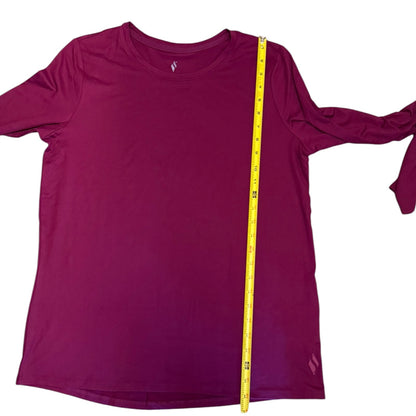 A purple long-sleeve athletic shirt laid flat on a white background, with a yellow tape measure placed vertically along the side to show the garment's width.