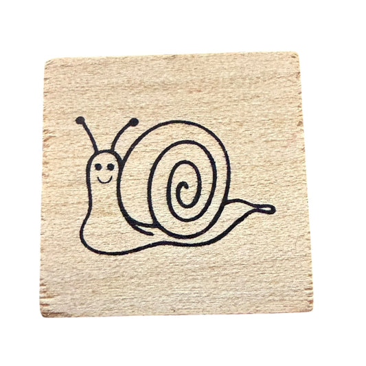 A square natural wood block featuring a simple black line art illustration of a smiling snail, shown against a plain white background.
