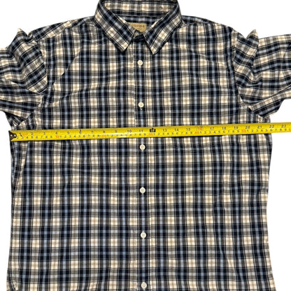 A short-sleeve plaid button-up shirt laid flat on a white background, with a yellow tape measure stretched horizontally across the chest to show the width.