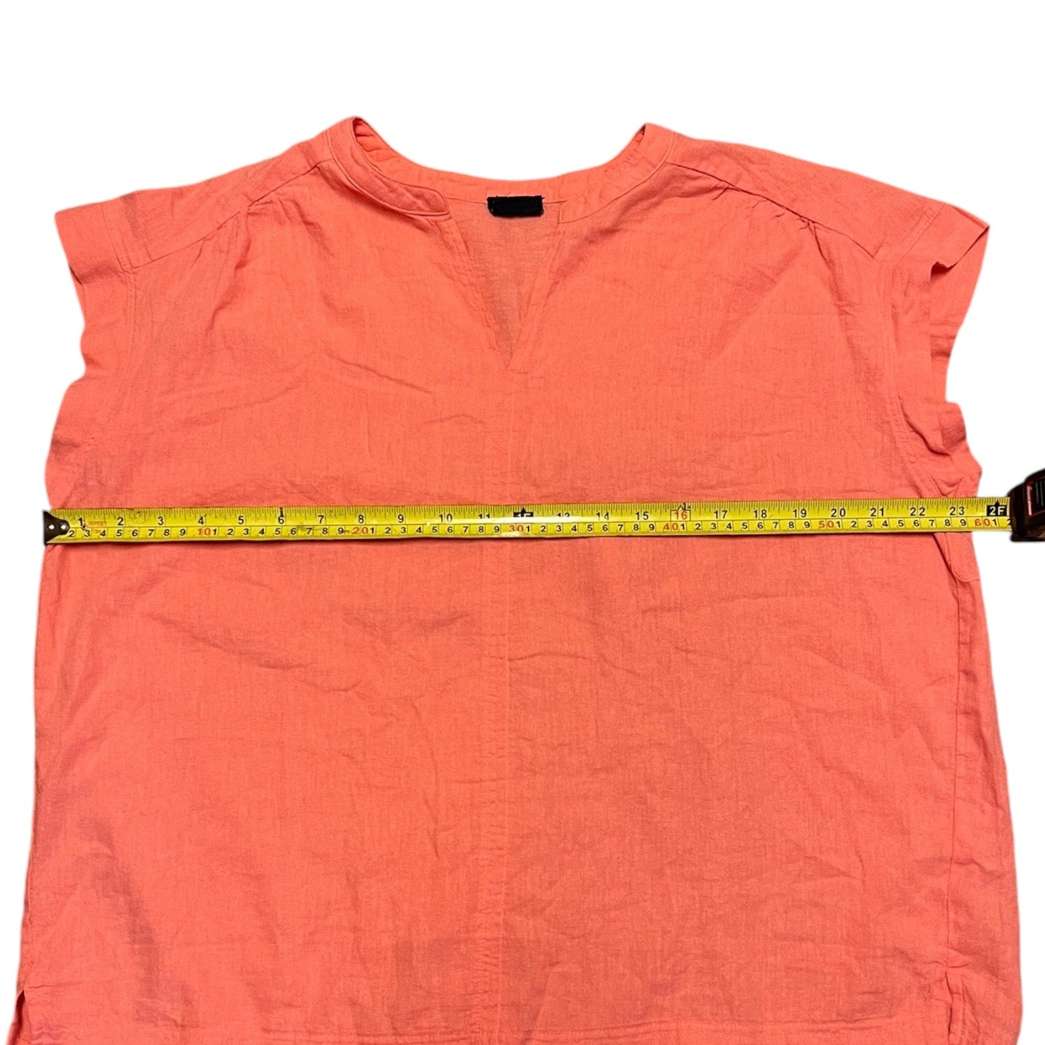Coral sleeveless top with a measuring tape across it on a white background