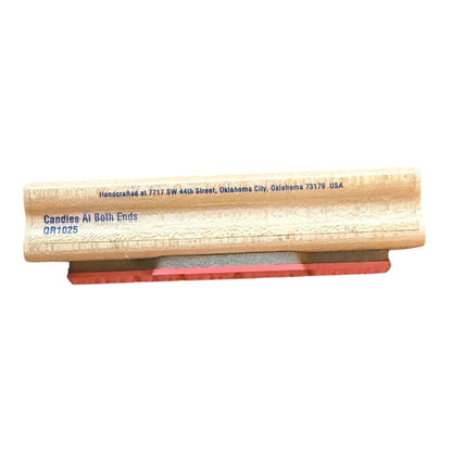 A wood rubber stamp, featuring blue printed text with the brand 'Candles At Both Ends' and a red rubber stamp head, shown against a plain white background.