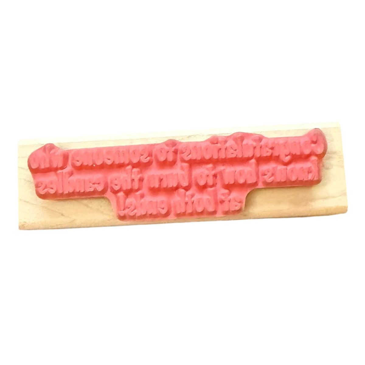 A pink rubber stamp with raised text on a light wood block, shown against a plain white background.